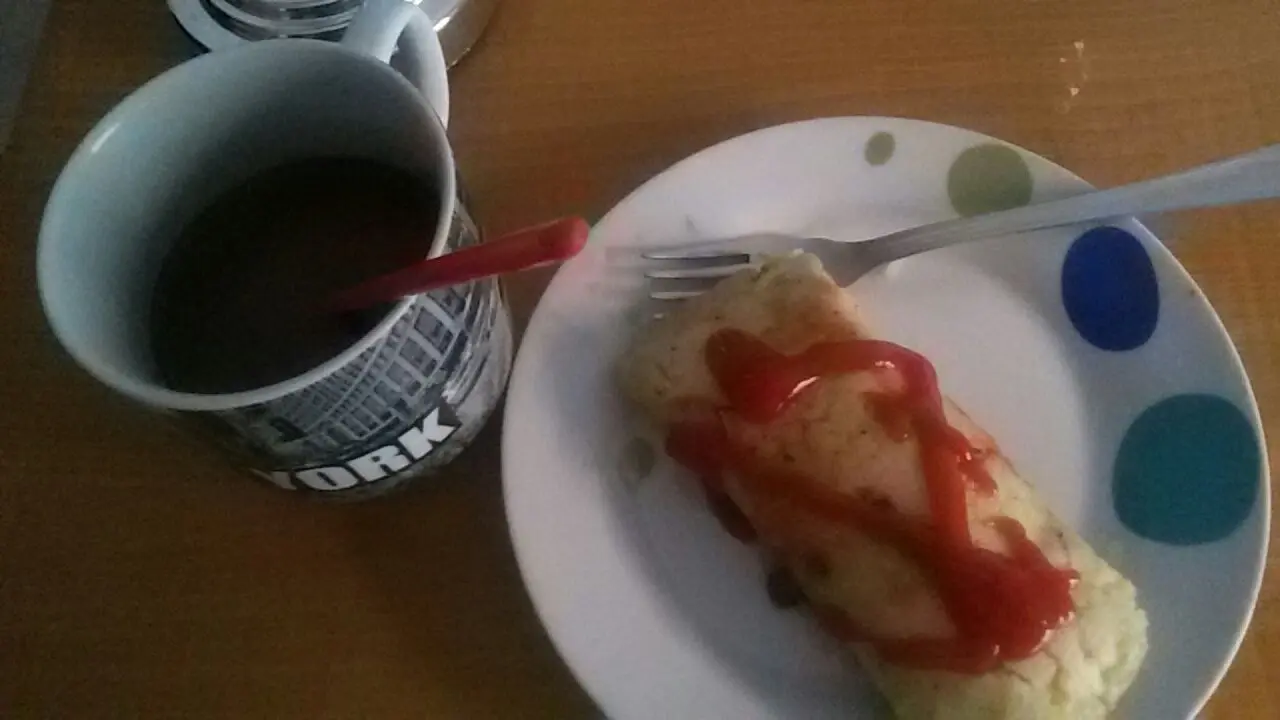 Plato blanco con un tamal hondureño ya sin hoja, con salsa de tomate encima y un tenedor, junto a una taza de café