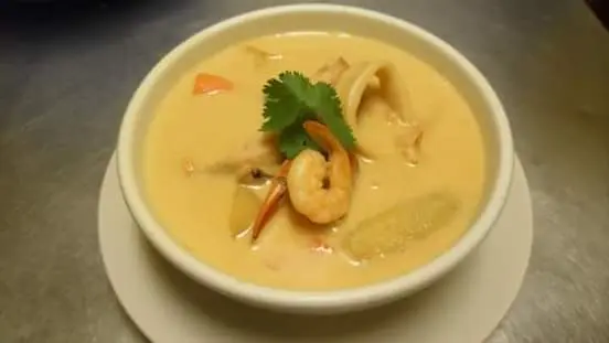 Plato hondo de sopa de caracol con leche de coco, trozos de caracol, camarones, zanahoria y una ramita de culantro encima