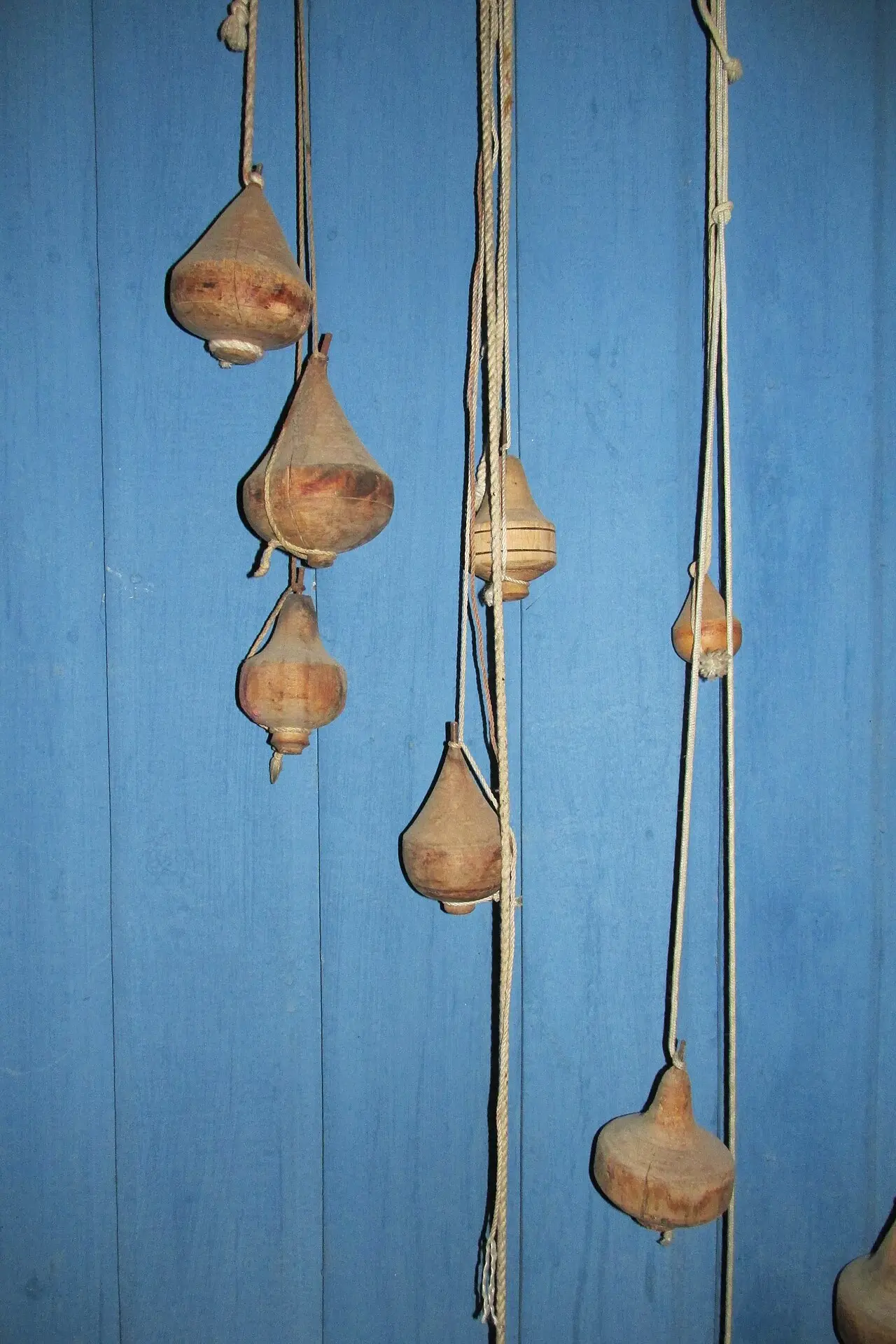 Trompos de madera colgados de sus cuerdas frente a una pared de tablas pintada de azul